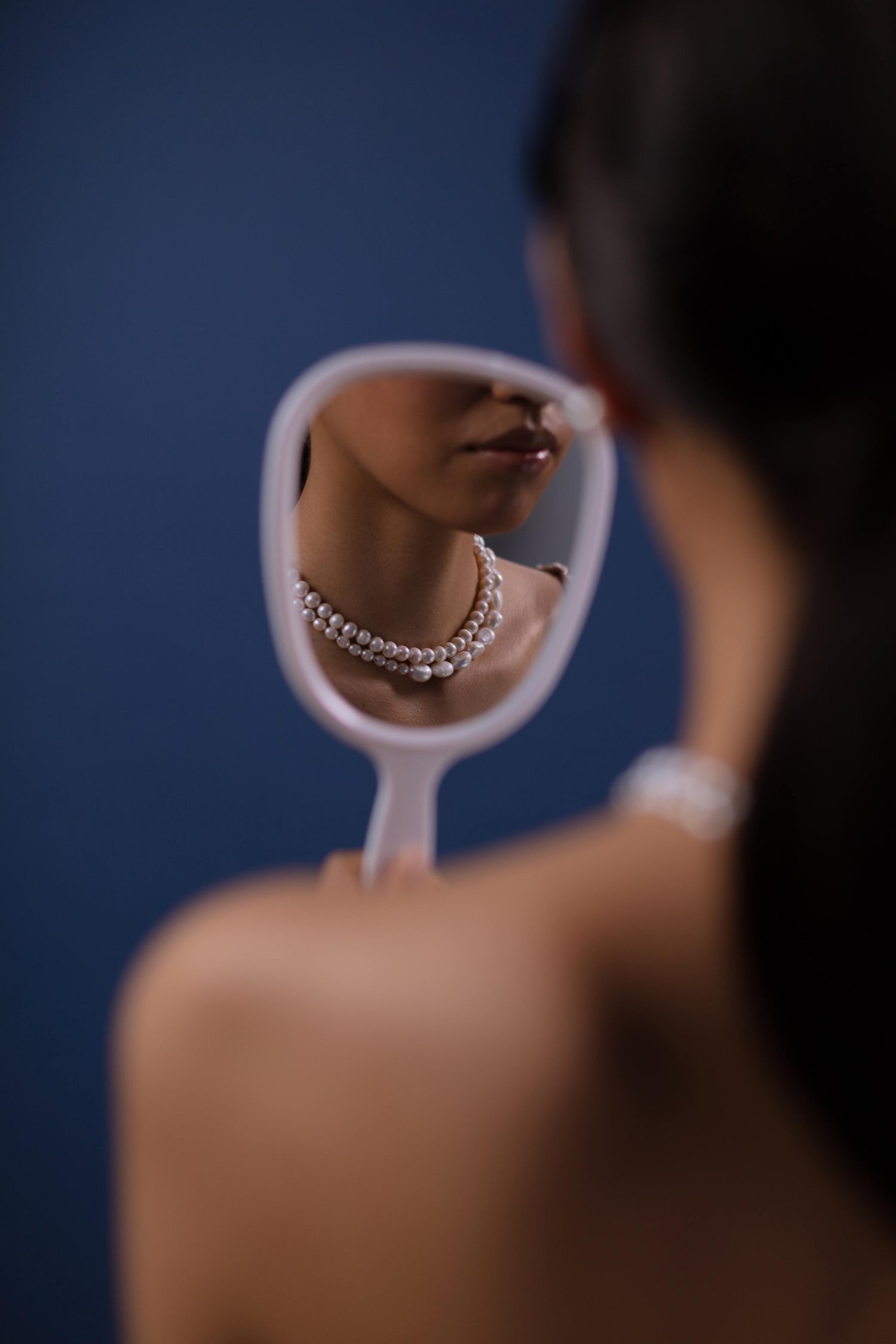A woman wearing a pearl necklace looking in the mirror