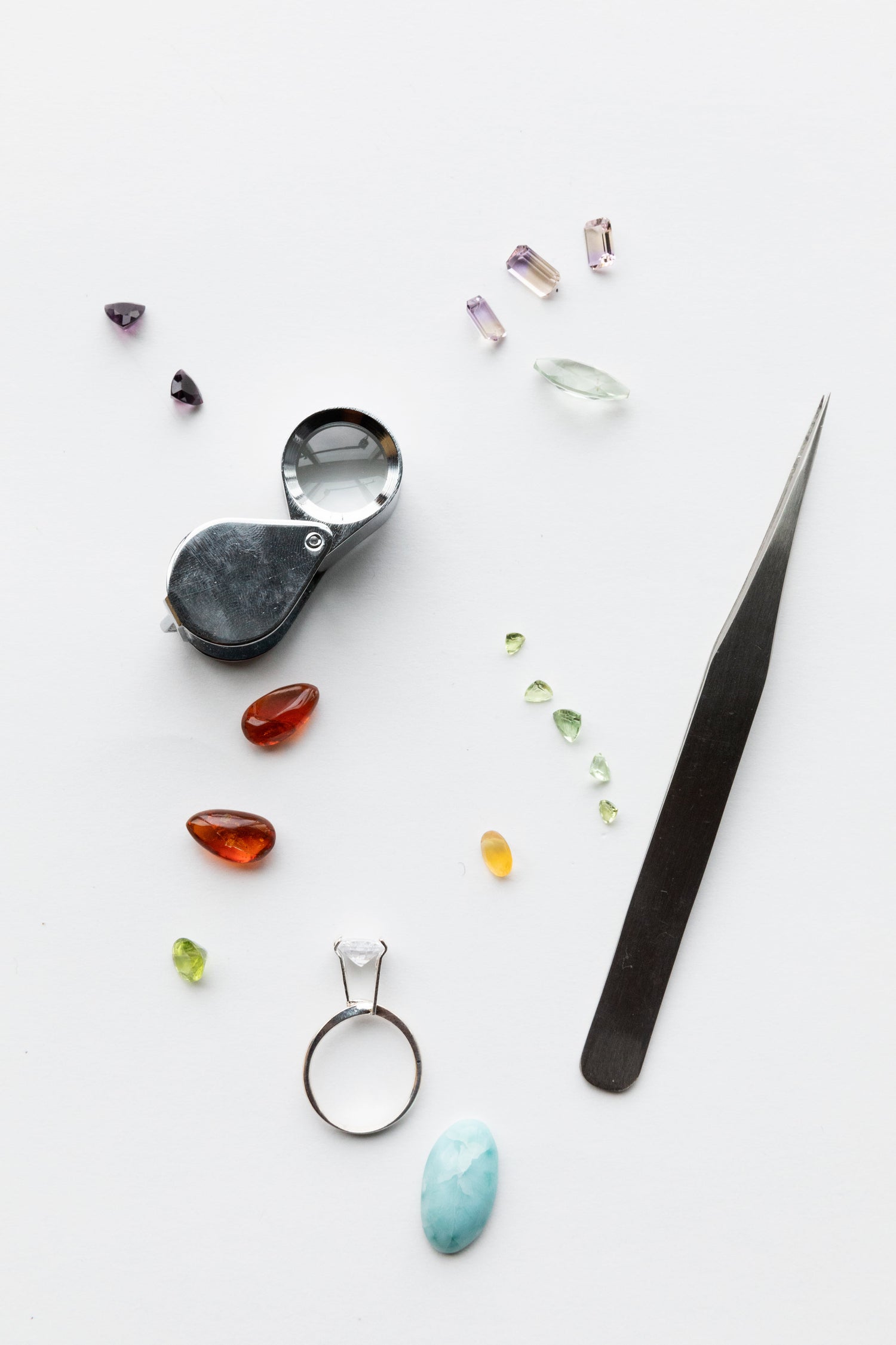 Different coloured gemstones, a ring, a loupe, and a tweezer